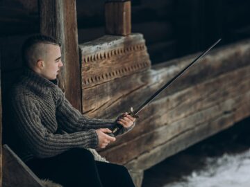 Portrait of strong viking warrior sharpening his sword, scandinavian viking cosplay