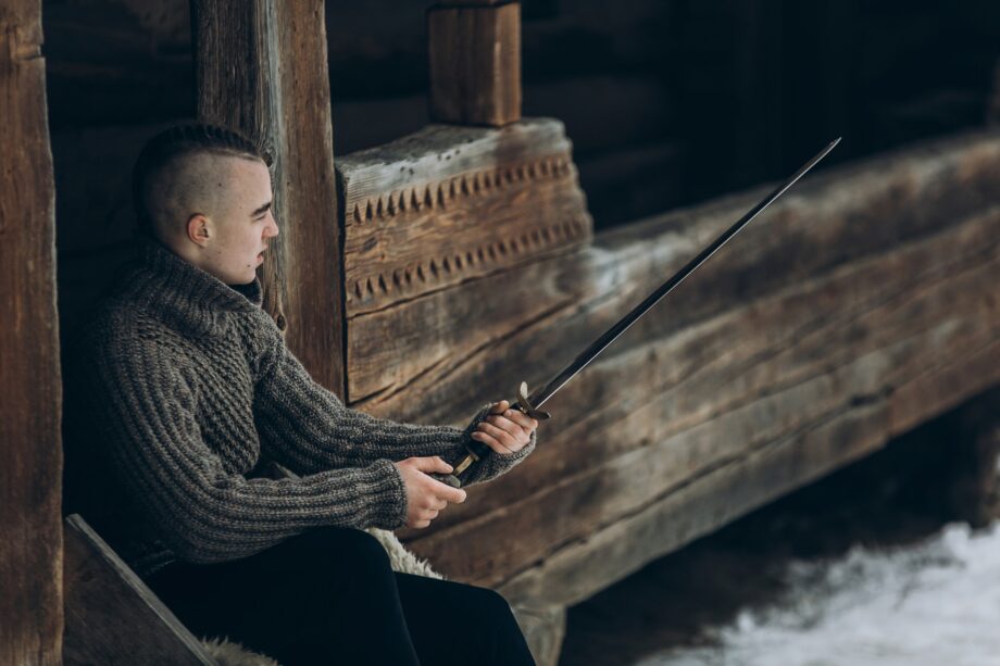 Portrait of strong viking warrior sharpening his sword, scandinavian viking cosplay