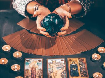 Tarot reader with tarot cards.Tarot cards face down on table near burning candles and crystal ball.