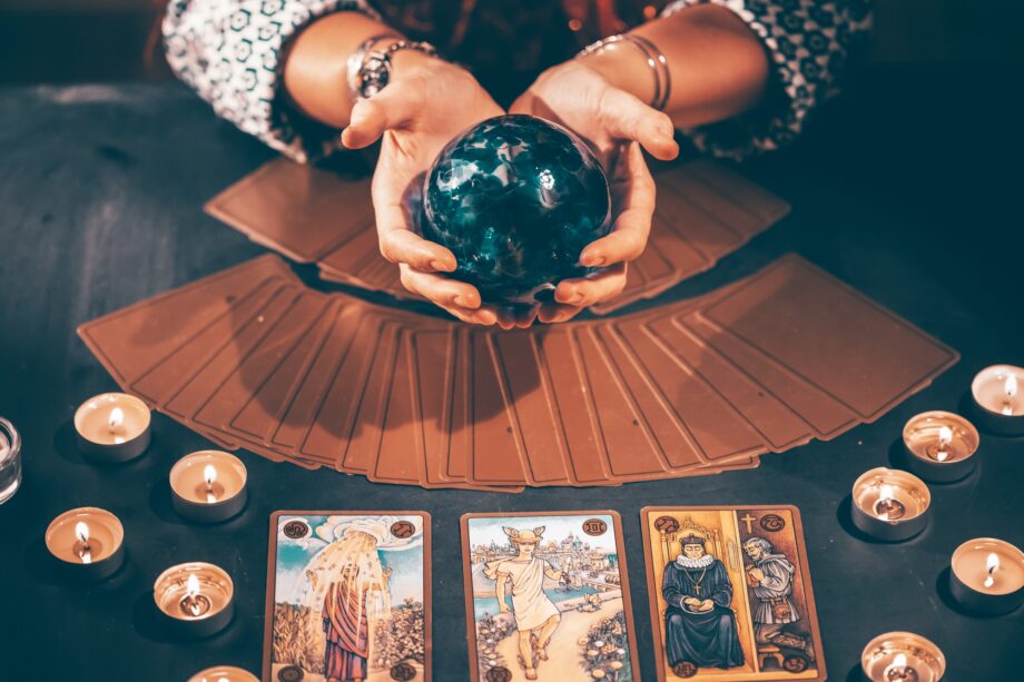 Tarot reader with tarot cards.Tarot cards face down on table near burning candles and crystal ball.